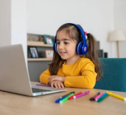 girl sitting at a desk with headphones on and looking at a laptop with markers on the desk next to her